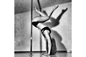 Black and White photo of jessica in a handstand against the pole, wearing a black criss cross bra